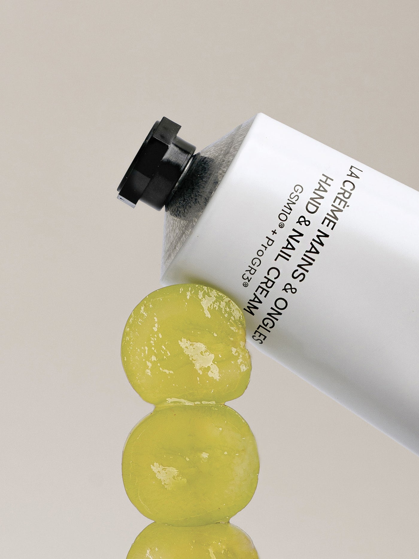 Tubo de crema de manos con uvas sobre un fondo neutro