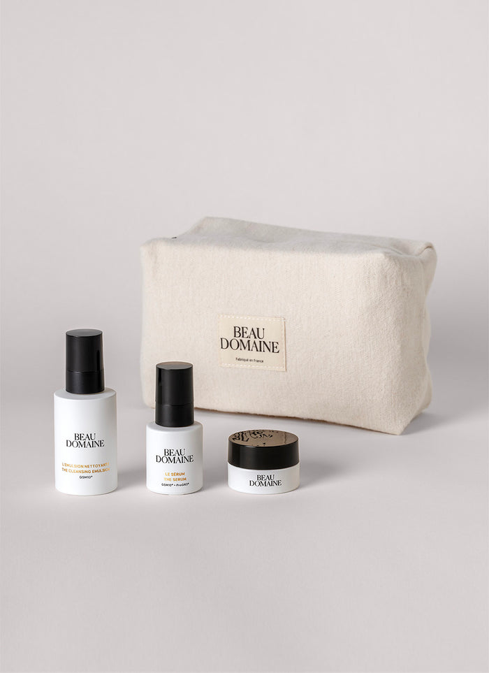 Set de cosmética con frascos y un tarro frente a una bolsa 'Beau Domaine' sobre fondo gris claro